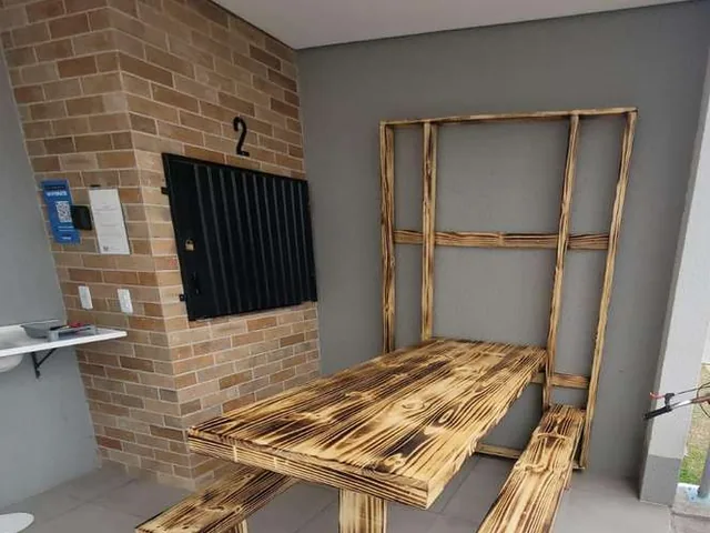 Espaço de churrasqueira com mesa e bancos de madeira e estrutura em construção
