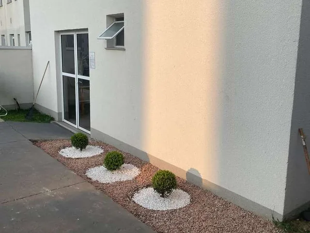 Canteiro de jardinagem com brita branca e arbustos moldados ao lado da fachada do prédio