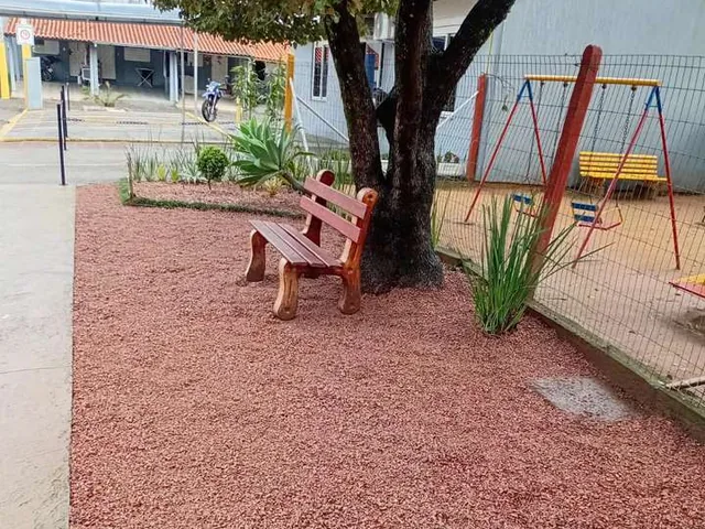 Área de recreação com piso de casca de pinus, banco de madeira e balanços sob a árvore