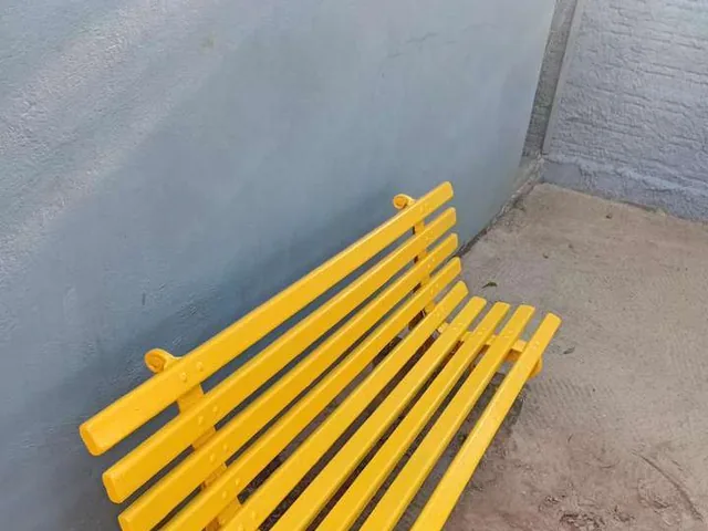 Banco de área comum recém-pintado em amarelo, ainda secando no pátio